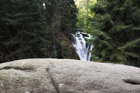 September in Karkonosze, waterfall on a mountain river in spruce forest visible behind a large rock, autumn landscapeの写真素材