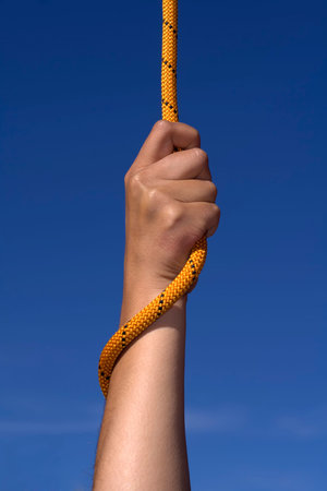 Hand with an orange rope on sky background