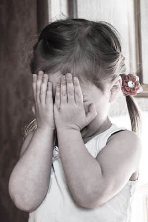 a frightened three-year-old girl covers her face with her handsの写真素材