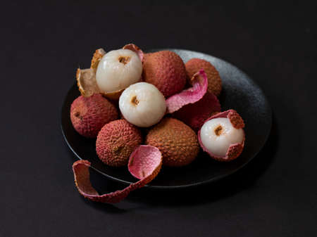 Lychee fruit on a black plate on a black background. Bowl of lychees with peels of lychee. Exotic fruit. Close up.の写真素材