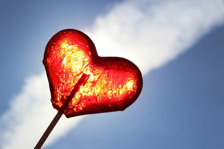 Red Lollipop on blue sky background. Heart shaped lollipopの写真素材
