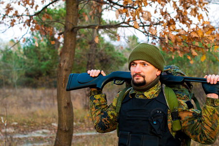 A man in uniform with a rifle in the autumn forest