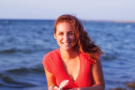 Young girl in a red dress smiling on the background of the seaの写真素材