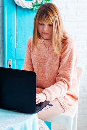 A girl student working with laptop. Girl freelancer with a computer in a home interior. Woman online buyer looks at the laptop screen.の写真素材