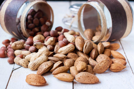 Hazelnuts almonds and peanuts scattered from the jars on a wooden table.の写真素材