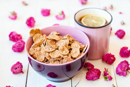 Romantic breakfast on white wooden background with flakes, tea with lemon and dry rosesの写真素材