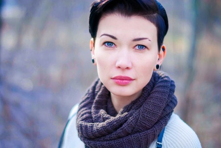Calm beautiful girl with blue eyes and short black hair in knitted scarf.の写真素材