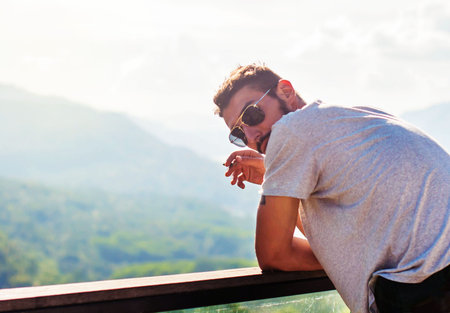 A handsome young man smokes with a view of the mountains
