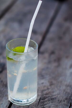A glass of lemonade and a straw on a wooden table. Alcohol cocktail with lime and tonic on a rough wooden background.の写真素材