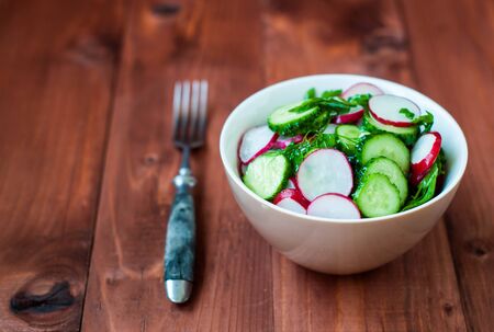 Summer salad of cucumbers and radish. Dietary salad from radish, cucumber, greens, and olive oil. Vegetable salad with parsley, dill and green onion. Fresh vegetable salad from a radish on a wooden table.の写真素材