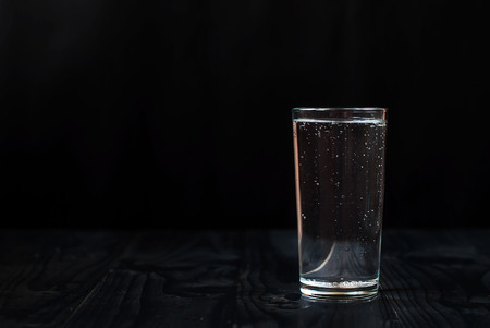 Just a glass of water on a dark wooden table. Mineral water in a glass on a black background. A glass with water.の写真素材
