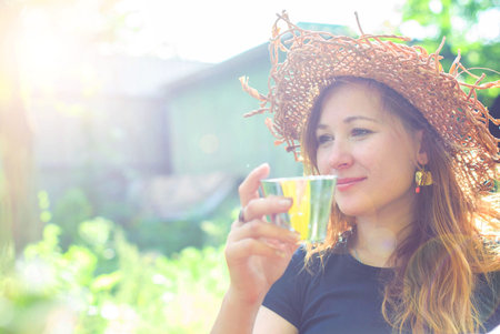 Beautiful young girl in a straw hat with a glass of drink in a summer garden.