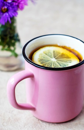 A pink mug with black tea and lemon and a glass vase with flowers.の写真素材
