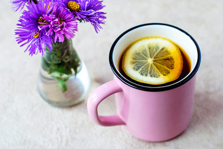 A pink mug with black tea and lemon and a glass vase with flowers.の写真素材