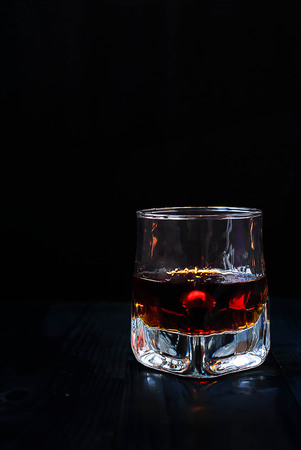 A glass of whiskey on a black background and a wooden tableの写真素材