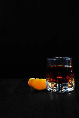 A glass of whiskey with an orange slice on a black background and a wooden tableの写真素材