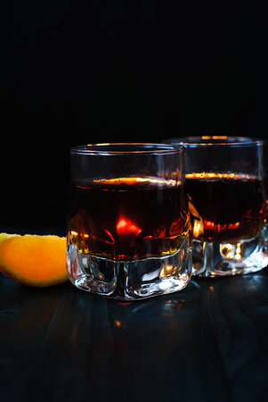 Two glasses of whiskey or cognac with an orange slice on a black background and a wooden tableの写真素材
