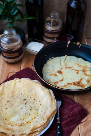Russian pancakes on a plate and a frying pan with pancakes with sour cream and raspberry jamの写真素材