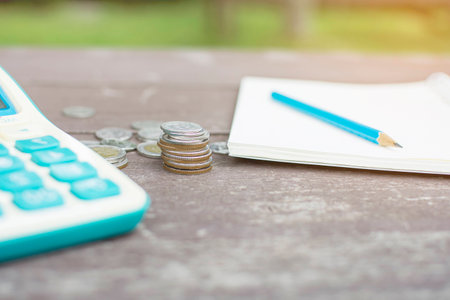 Selective focus of stack of coins with blue pencil on blank notebook finance and calculator to calculate the balance on the wooden tableの写真素材