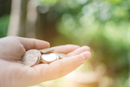 Thai coin on Asian woman hand with bokeh tree background, saving money concept