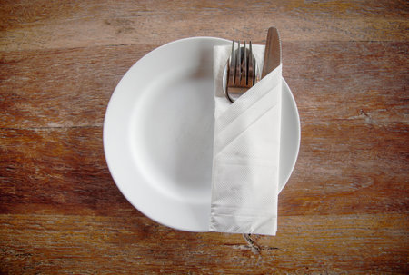 Top view of white circle plate with spoon, fork, knife and napkin on wooden table