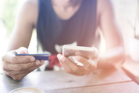 Soft focus Hipster Asian manâ€™s hands using smart phone and holding a credit card for online...