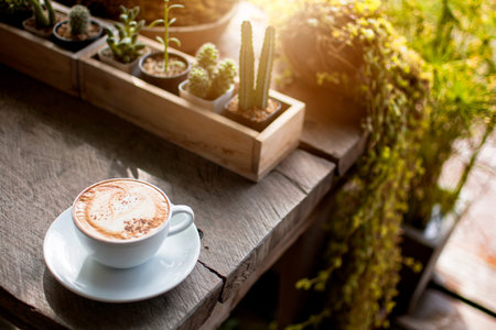White cup of hot coffee with the white cream and white plate on the wooden table in the restaurant...