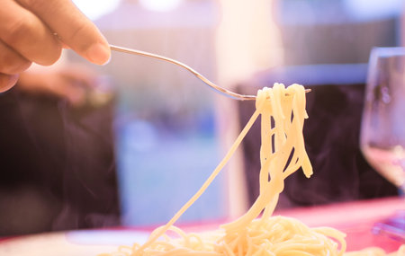 Hand lifted Italian spaghetti steaming by strong fork for large serving in the restaurant with...