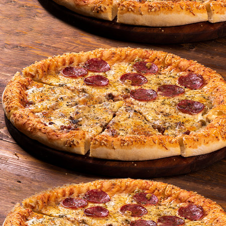 Three pepperoni pizzas on a wooden tableの写真素材