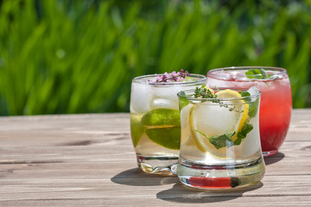 Three glasses of refreshing drink with herbs on a wooden table in the garden