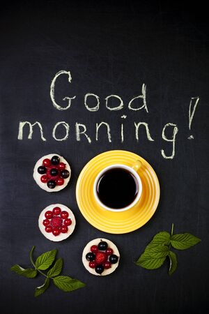 Cup of coffee with three cakes on a black background and a "good morning" textの写真素材
