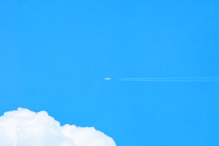 Airplane flying with contrail and white clouds in blue sky. Minimal background.の写真素材