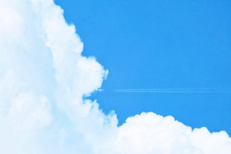 Airplane with white contrail flying into the big clouds with blue sky. Minimal background.