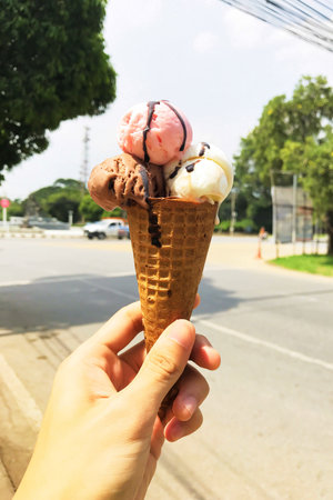 Hand holding Chocolate, Vanilla and Strawberry Ice cream cone in summer or hot weather.