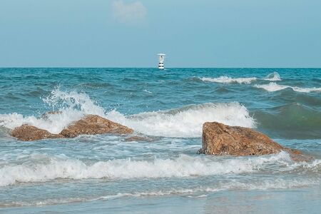 Lighthouse on the sea with Thailand flag and Sea wave and Splashes  hits the stone on the beach. Pastel tone.の写真素材