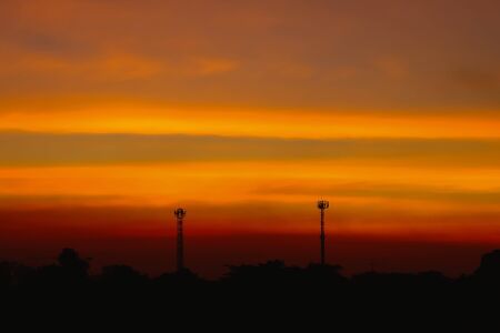 Silhouette of Beautiful sunset with television antenna or telecommunications towers have a lot of different antennas, Orange sky with sun and clouds. Nature background.の写真素材