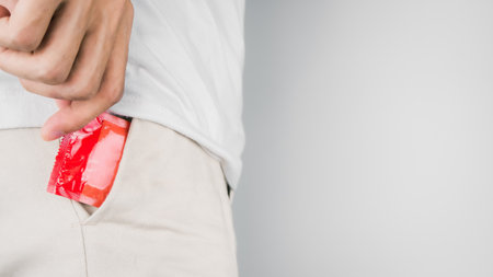 Man wearing white t-shirt and hand pulled red condom out of the pant pocket. Concept of Safe sex. Reduce of pregnancy and sexually transmitted disease.の写真素材