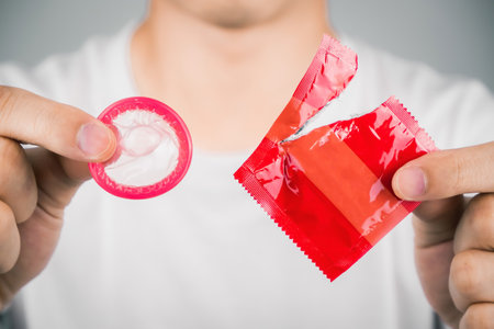 Man wearing white t-shirt and hand tearing a red condom. Concept of Safe sex. Reduce of pregnancy and sexually transmitted disease.の写真素材