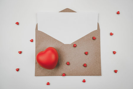 Blank white paper is placed on open brown paper envelope with red heart. Top view of Craft paper envelope on white background. Valentine's day conceptの写真素材
