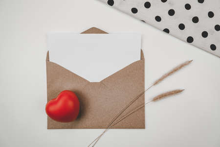 Blank white paper is placed on open brown paper envelope with red heart, Bristly foxtail dry flower, White cloth on white background. Valentine's day conceptの写真素材