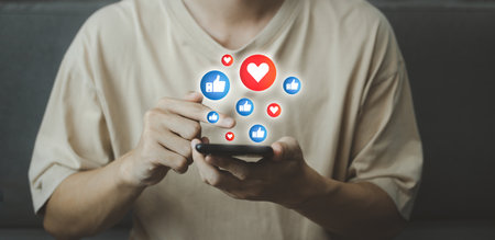 Chat and notification on smartphone with virtual red heart and blue like emoji social media icon. Man using smartphone on vacation with hologram. Social media and digital online concept.の写真素材
