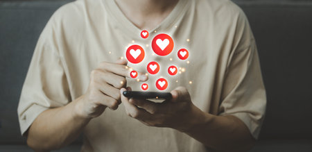 Chat and notification on smartphone with virtual red heart emoji social media icon. Man using...