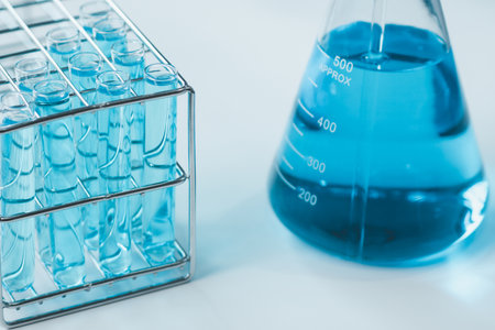 Test tubes and erlenmeyer flask filled with blue sample chemicals in chemistry science laboratory. Glassware in medical research. Scientific lab for Biotechnology.の写真素材
