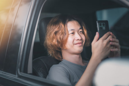 Young asian man with long hair hand use smartphone in car at parking. Transport, vehicle and technology conceptの写真素材