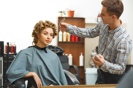 Hairdresser doing hairstyle for young beautiful woman