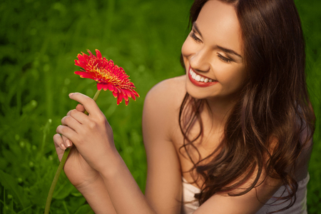 Beautiful Girl With Gerbera Flower Enjoying Nature. Spring Meadow. Grass and Flowersの写真素材