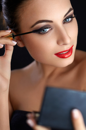 Portrait of young woman applying mascara.  Mascara Brush. Red Lipsの写真素材