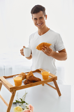 Young handsome loving man making romantic breakfast in the morningの写真素材