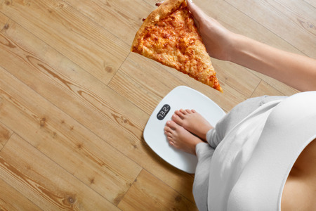 Diet And Fast Food Concept. Overweight Woman Standing On Weighing Scale Holding Pizza. Unhealthy Junk Food. Dieting, Lifestyle. Weight Loss. Obesity. Top Viewの写真素材