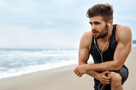 Portrait Of Athletic Man With Fit Muscular Body Resting After Jogging On Beach. Tired Exhausted Male Runner Taking A Break, Breathing After Running Workout Outdoor Near Ocean. Sports, Fitness Conceptの写真素材